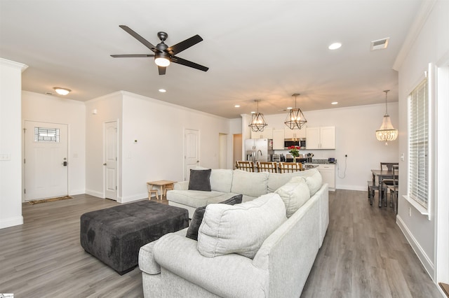 living room with ornamental molding, ceiling fan with notable chandelier, and light hardwood / wood-style flooring