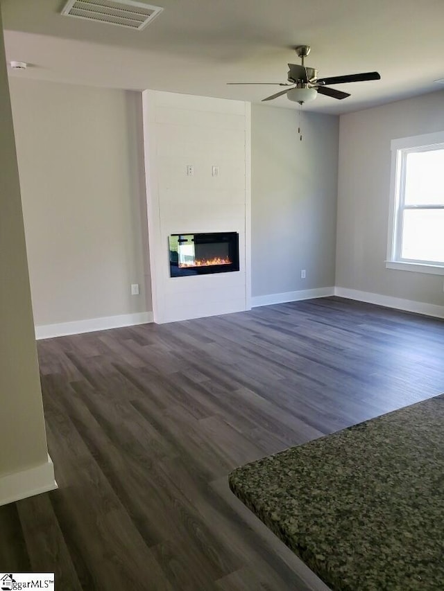 unfurnished living room featuring dark wood-type flooring and ceiling fan