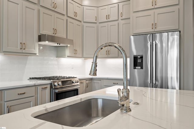 kitchen with gray cabinets, appliances with stainless steel finishes, sink, backsplash, and light stone countertops