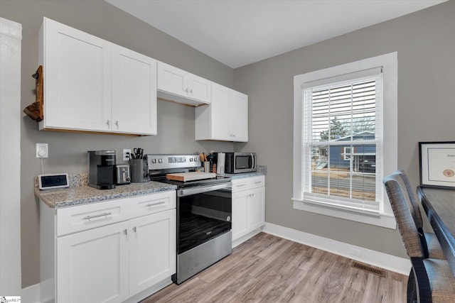 kitchen with stainless steel appliances, white cabinetry, light stone counters, and light wood-type flooring