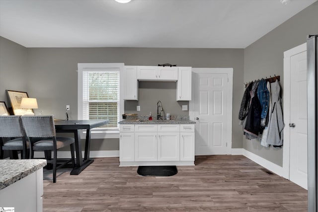 kitchen with white cabinetry, sink, light hardwood / wood-style flooring, and light stone countertops