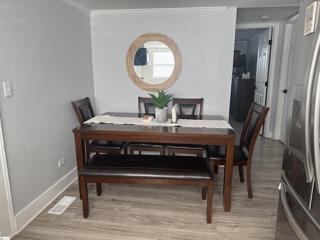 dining room with ornamental molding and light hardwood / wood-style flooring