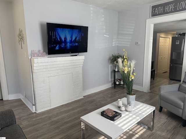 living room with a brick fireplace, a textured ceiling, and dark hardwood / wood-style flooring