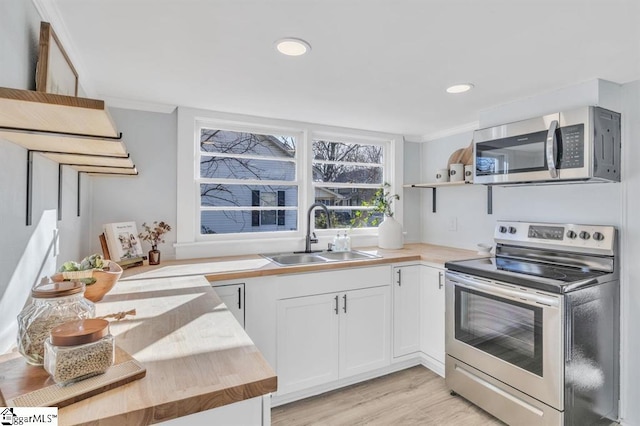 kitchen with butcher block counters, sink, crown molding, appliances with stainless steel finishes, and white cabinets