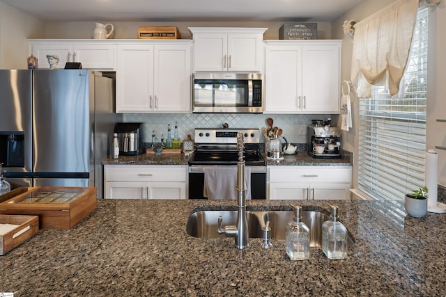 kitchen with tasteful backsplash, appliances with stainless steel finishes, white cabinets, and dark stone counters