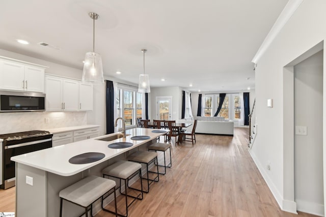 kitchen featuring sink, range with gas cooktop, white cabinetry, decorative light fixtures, and a kitchen island with sink