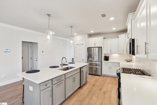 kitchen featuring sink, hanging light fixtures, appliances with stainless steel finishes, an island with sink, and white cabinets