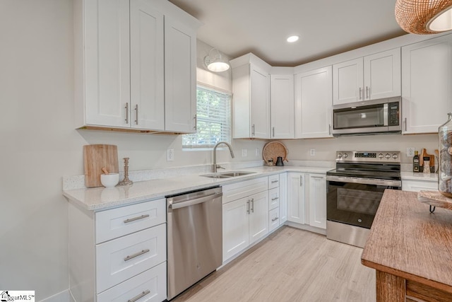 kitchen with sink, appliances with stainless steel finishes, white cabinetry, light stone counters, and light wood-type flooring