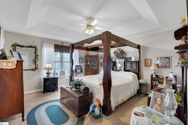 bedroom with a textured ceiling, light colored carpet, a raised ceiling, and ceiling fan