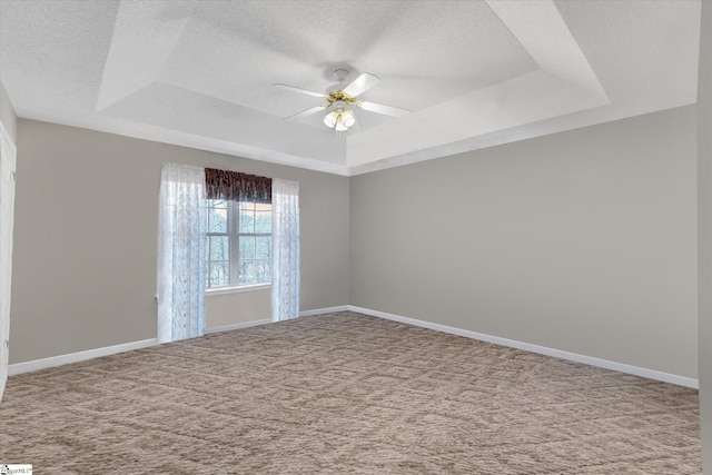 carpeted empty room featuring a textured ceiling, ceiling fan, and a tray ceiling