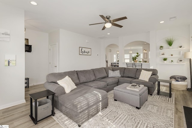 living room featuring built in shelves, light hardwood / wood-style flooring, and ceiling fan