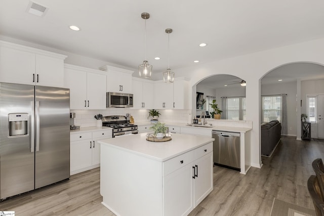 kitchen featuring appliances with stainless steel finishes, white cabinets, backsplash, hanging light fixtures, and a center island