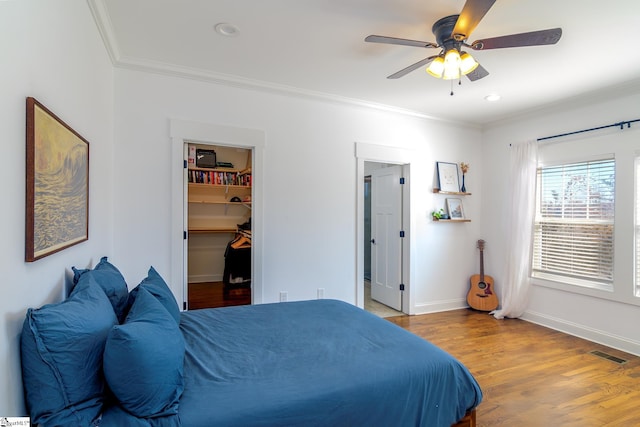 bedroom featuring crown molding, a spacious closet, a closet, ceiling fan, and light hardwood / wood-style floors