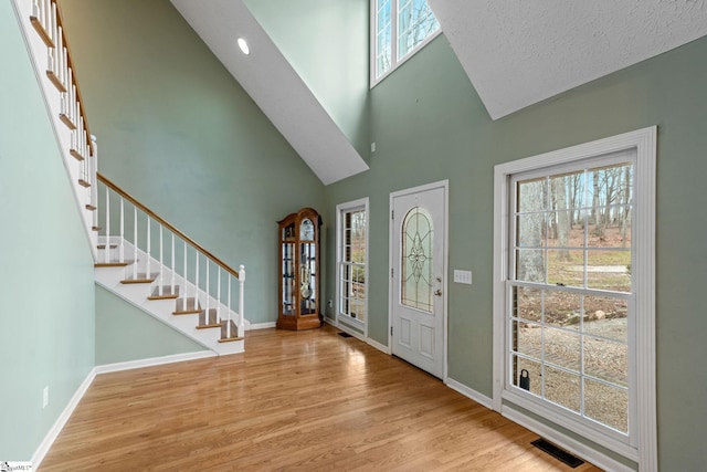 entryway featuring high vaulted ceiling, a textured ceiling, and light wood-type flooring