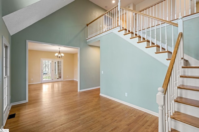 stairway with an inviting chandelier, wood-type flooring, and high vaulted ceiling