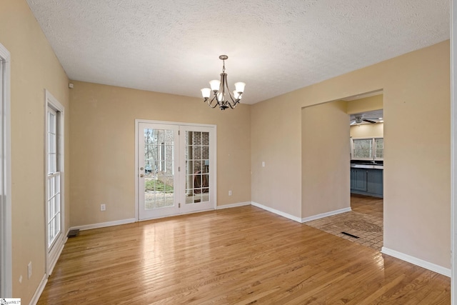 empty room featuring a textured ceiling, a chandelier, and light wood-type flooring