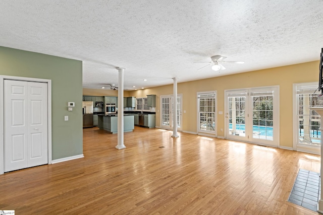 unfurnished living room with decorative columns, a textured ceiling, ceiling fan, and light hardwood / wood-style flooring