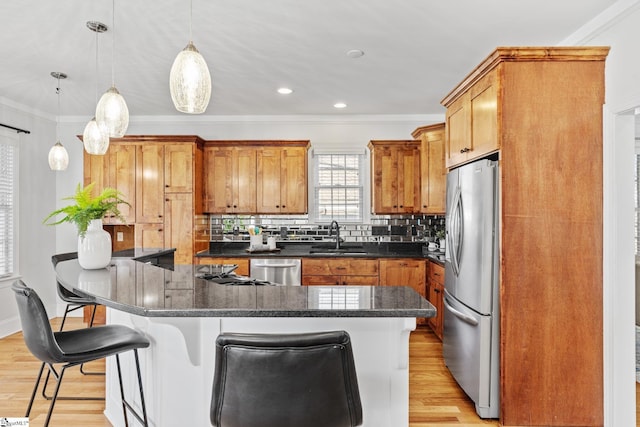 kitchen with appliances with stainless steel finishes, a breakfast bar area, hanging light fixtures, and light hardwood / wood-style flooring