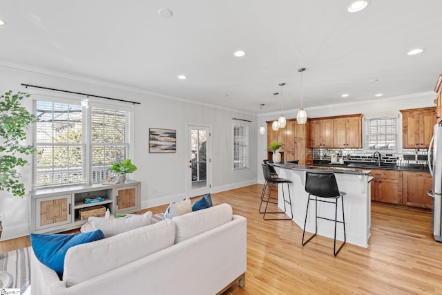 living room with ornamental molding, a wealth of natural light, sink, and light wood-type flooring