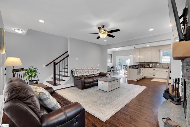 living room with dark wood-type flooring, ceiling fan, and a stone fireplace