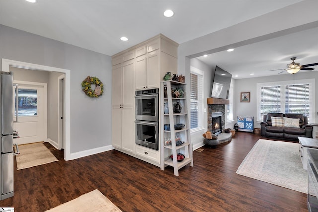 kitchen with ceiling fan, a fireplace, stainless steel appliances, and dark hardwood / wood-style floors