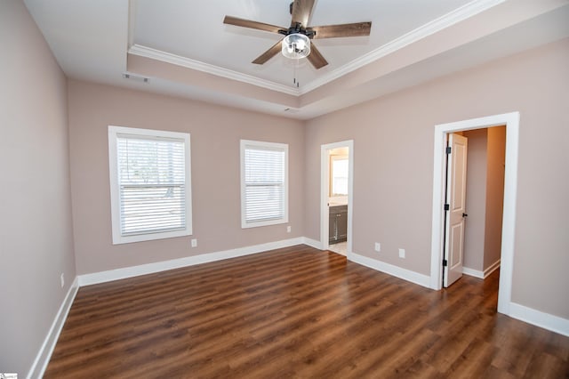 unfurnished bedroom featuring crown molding, ensuite bath, a tray ceiling, dark hardwood / wood-style flooring, and ceiling fan