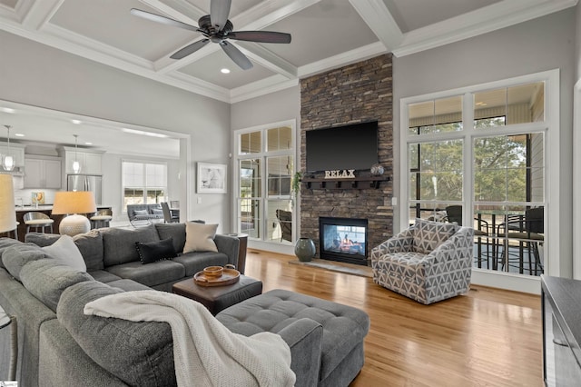 living room with a stone fireplace, beamed ceiling, coffered ceiling, light hardwood / wood-style floors, and crown molding