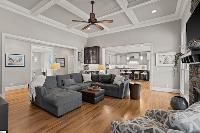 living room with a stone fireplace, hardwood / wood-style floors, beamed ceiling, coffered ceiling, and crown molding