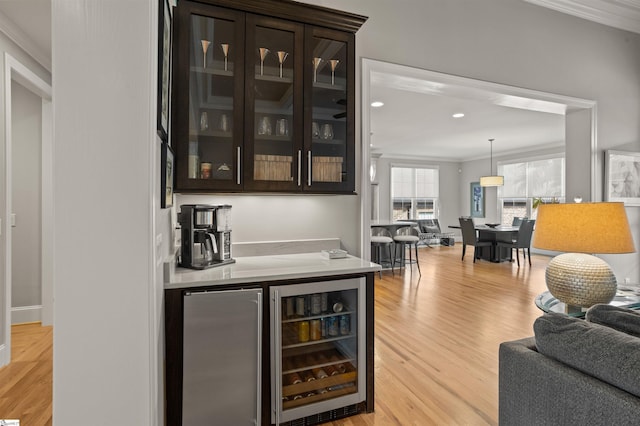 bar featuring crown molding, stainless steel refrigerator, dark brown cabinets, light hardwood / wood-style floors, and beverage cooler