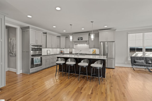 kitchen featuring crown molding, hanging light fixtures, appliances with stainless steel finishes, a kitchen breakfast bar, and gray cabinets