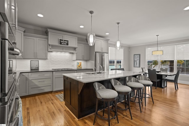 kitchen with appliances with stainless steel finishes, decorative light fixtures, an island with sink, sink, and gray cabinetry