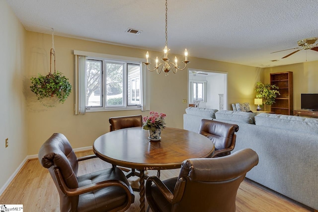 dining room featuring light wood-type flooring, ceiling fan with notable chandelier, and a textured ceiling