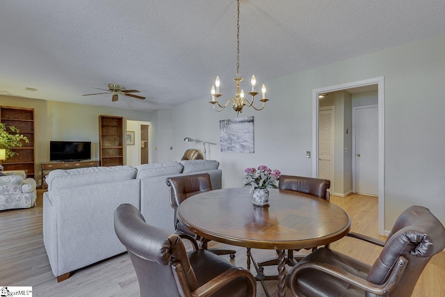 dining area with ceiling fan with notable chandelier, a textured ceiling, and light wood-type flooring