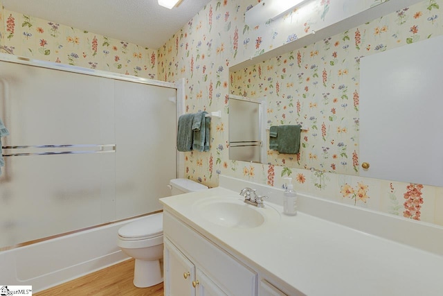 full bathroom featuring hardwood / wood-style floors, bath / shower combo with glass door, vanity, a textured ceiling, and toilet