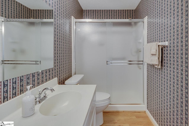 bathroom featuring vanity, wood-type flooring, a textured ceiling, a shower with shower door, and toilet