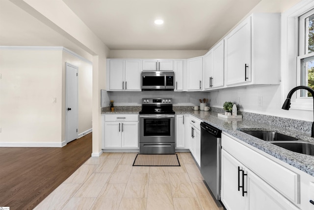 kitchen featuring stainless steel appliances, white cabinetry, light stone countertops, and sink