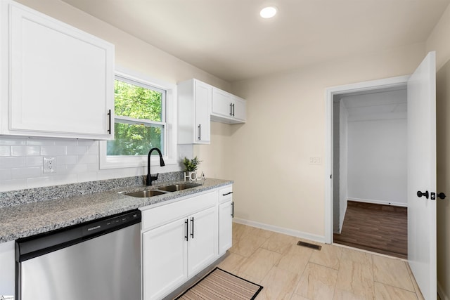 kitchen with tasteful backsplash, sink, white cabinets, stainless steel dishwasher, and light stone countertops