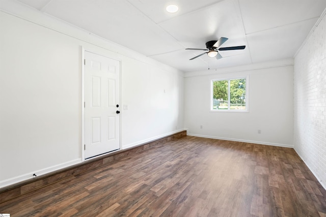 unfurnished room featuring dark hardwood / wood-style floors, ceiling fan, and brick wall