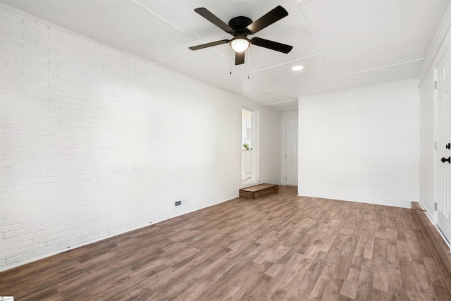 empty room with wood-type flooring, brick wall, and ceiling fan