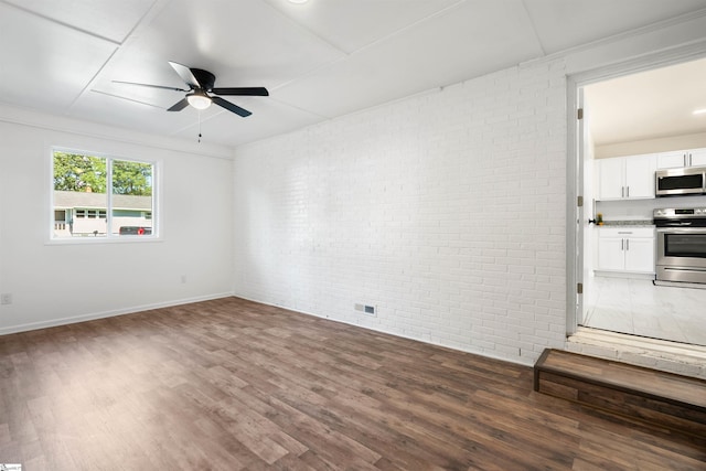 empty room featuring brick wall, dark wood-type flooring, and ceiling fan