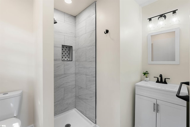 bathroom featuring vanity, a tile shower, and toilet