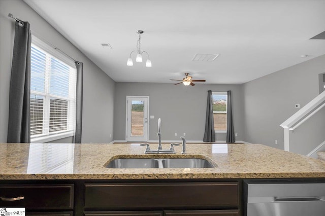 kitchen with ceiling fan with notable chandelier, sink, hanging light fixtures, dark brown cabinetry, and light stone countertops