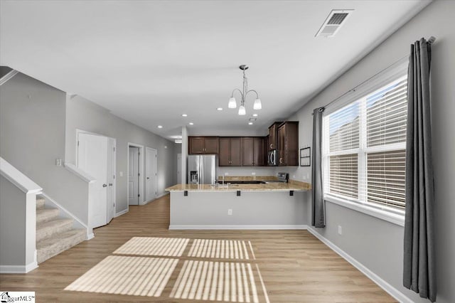 kitchen with hanging light fixtures, dark brown cabinets, stainless steel appliances, light hardwood / wood-style floors, and kitchen peninsula