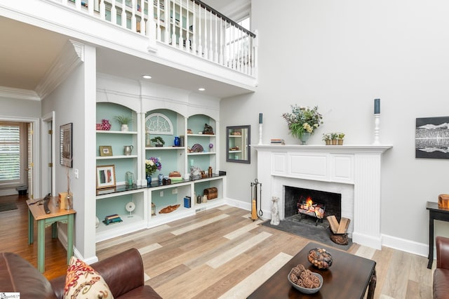 living room featuring a high ceiling, crown molding, built in shelves, and light wood-type flooring