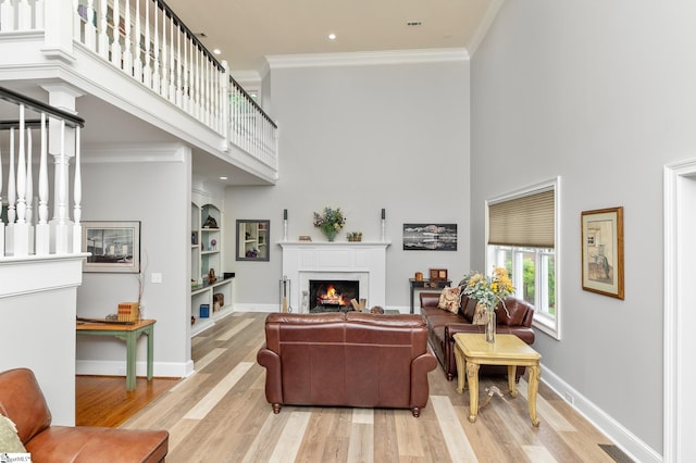 living room with crown molding, a towering ceiling, built in features, and light wood-type flooring