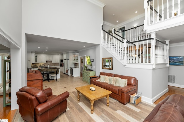 living room with a high ceiling, crown molding, and light hardwood / wood-style floors