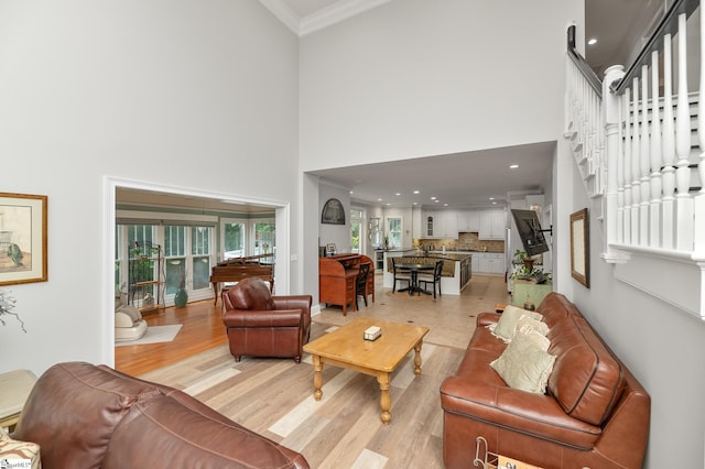 living room with a towering ceiling, ornamental molding, light hardwood / wood-style floors, and a healthy amount of sunlight