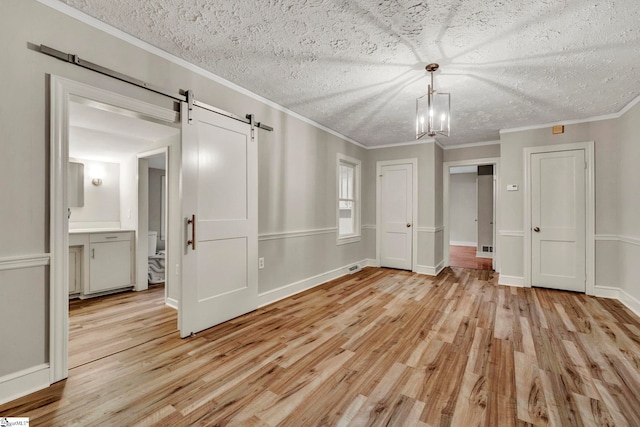 unfurnished bedroom featuring connected bathroom, crown molding, a barn door, and light wood-type flooring