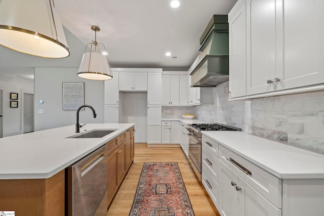 kitchen with sink, white cabinetry, appliances with stainless steel finishes, pendant lighting, and a kitchen island with sink