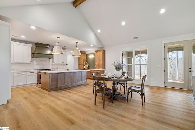 dining room with beamed ceiling, high vaulted ceiling, sink, and light hardwood / wood-style floors